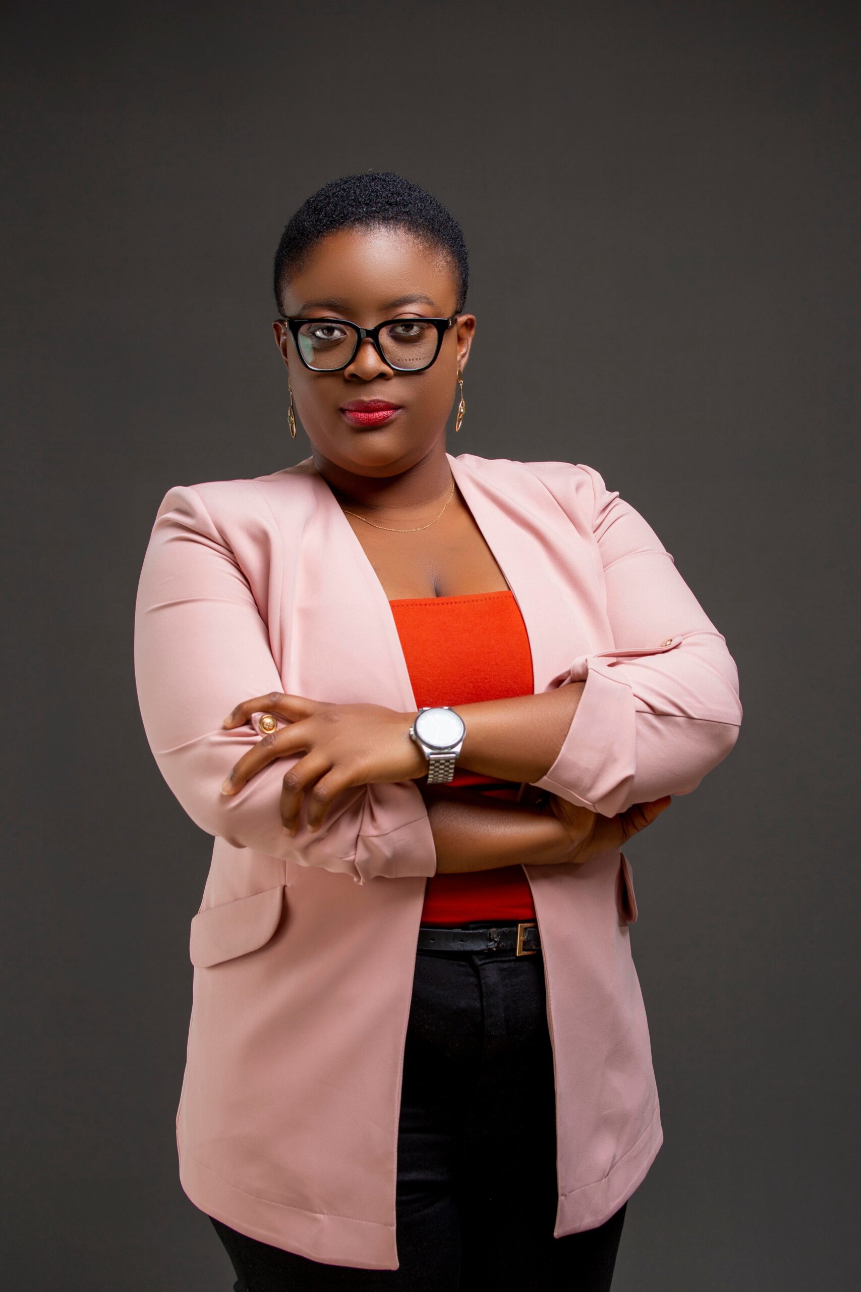 Portrait of a confident businesswoman in a pink blazer with arms crossed, wearing eyeglasses.