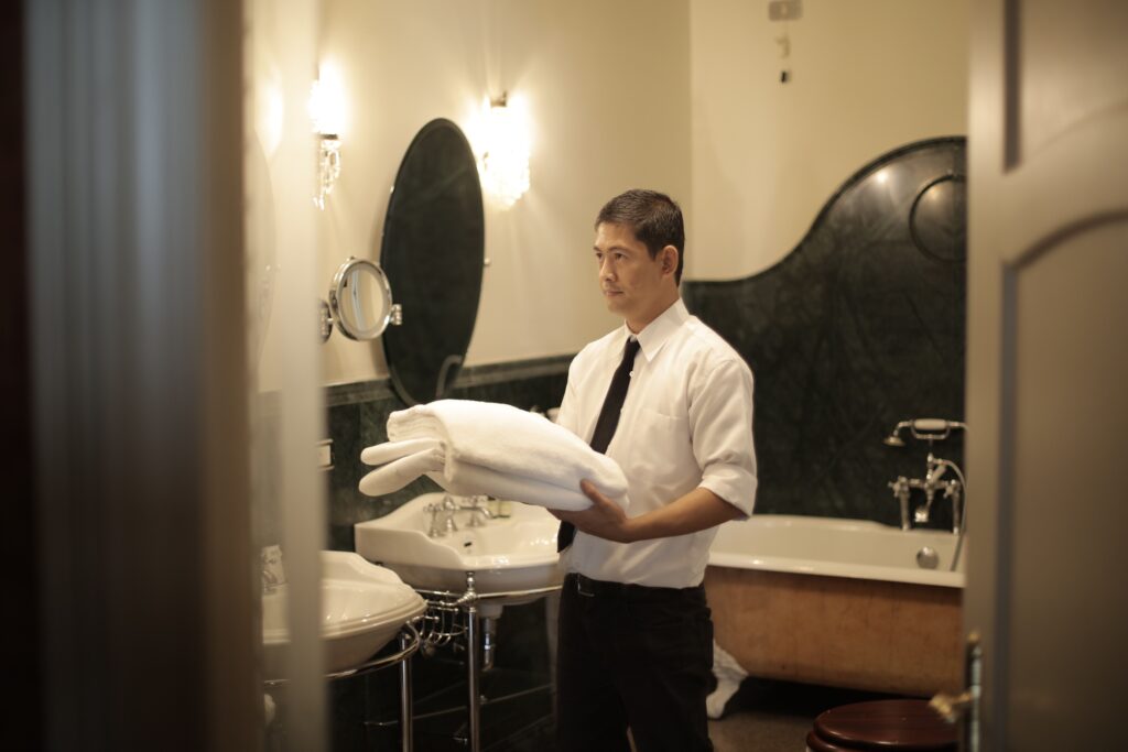 Side view of young male employee holding stack of white towels while standing in bathroom of luxury hotel