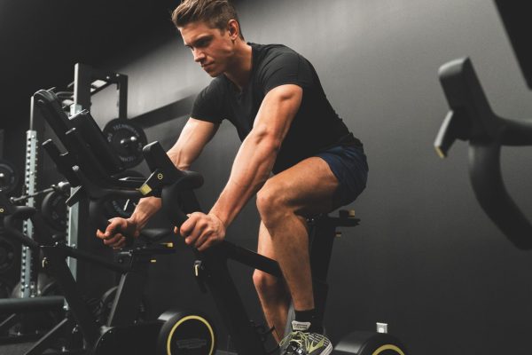 Muscular man biking indoors in gym setting, showcasing fitness and sportswear.