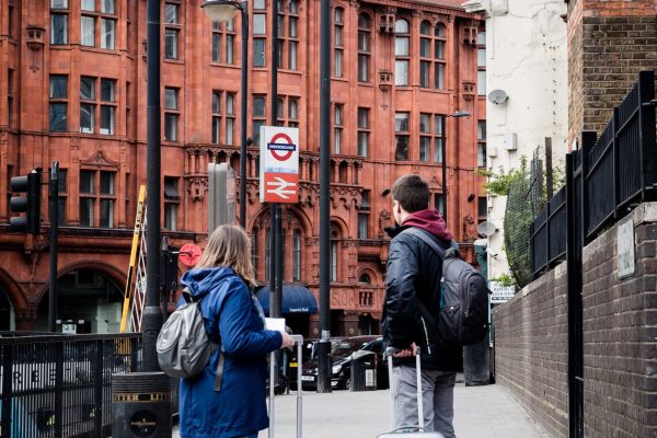 A couple with suitcases stands on a London sidewalk, showcasing urban travel and architecture.