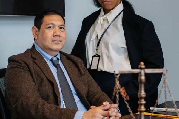 Focused young black woman in formal clothes standing near male ethnic colleague at wooden table with documents and justice scale during work in law firm
