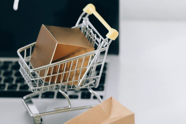 A miniature shopping cart with a parcel on a laptop symbolizes online shopping and e-commerce.